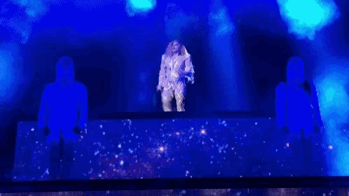 a woman is singing into a microphone on a stage with two men dancing in the background .