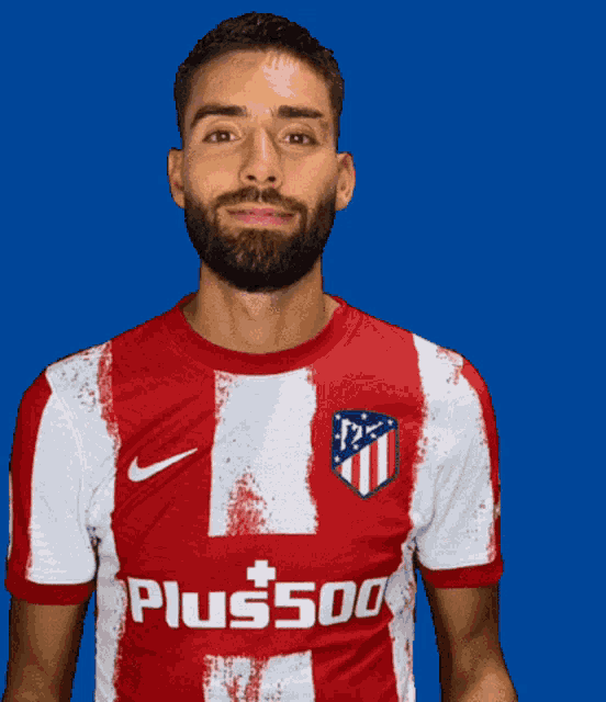 a man with a beard wears a red and white shirt that says plus500