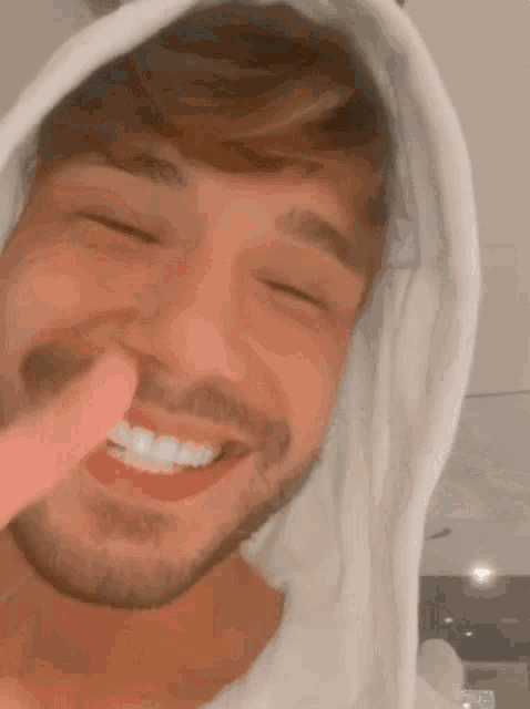 a man with a beard wearing a white hoodie smiles with his eyes closed
