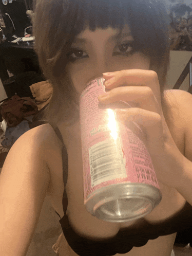 a woman in a black bra drinks from a pink can that says ' strawberry ' on it