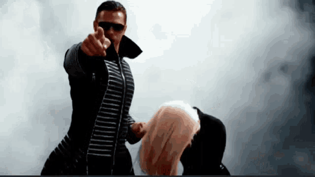 a man in sunglasses is pointing at a woman in a black jacket