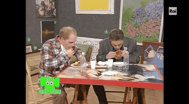 two men are sitting at a table with a green sign that says tele