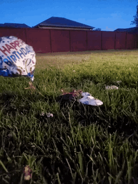 a happy birthday balloon in the grass with a fence in the background