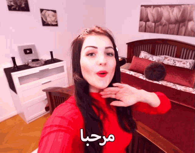 a woman in a red sweater is taking a selfie in a bedroom with arabic writing on it