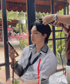 a man is sitting at a table getting his hair styled while looking at his cell phone