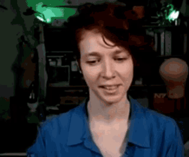 a woman with red hair is wearing a blue shirt and smiling in front of a green light .