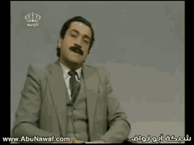 a man in a suit and tie is sitting in front of a diamond and the website www.abunawaf.com is visible