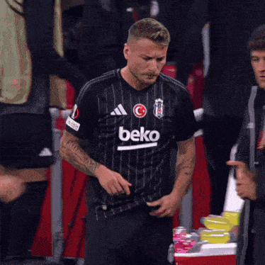 a man wearing a black beko jersey is standing in front of a cooler