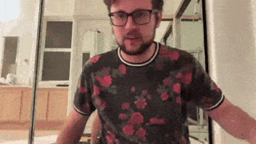 a man wearing glasses and a floral shirt is standing in front of a mirror in a room .