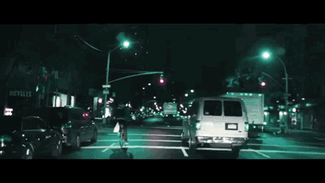 a white van is driving down a street at night with a sign that says cycles in the background