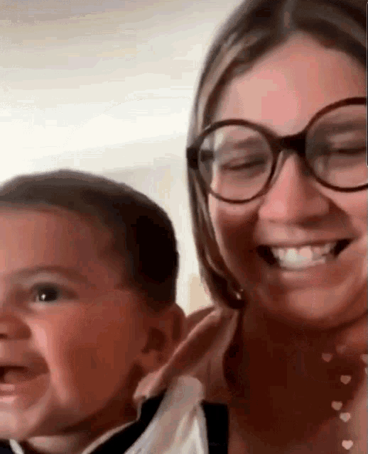 a woman wearing glasses is holding a baby and smiling at the camera .