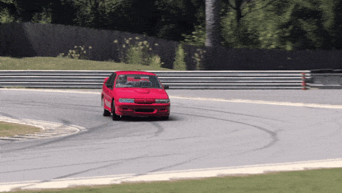 a red car is driving on a track with a fence behind it