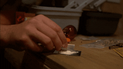 a man is sniffing a piece of cocaine on a table next to a warning sign