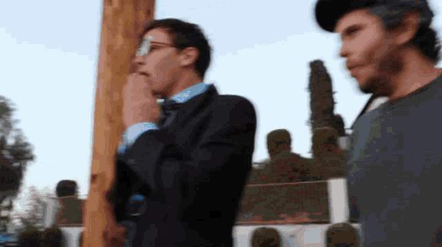 a man in a suit stands next to another man in a hat