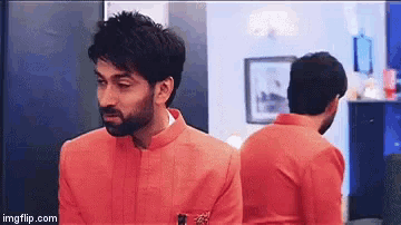 a man in an orange jacket is standing in front of a mirror looking at himself .