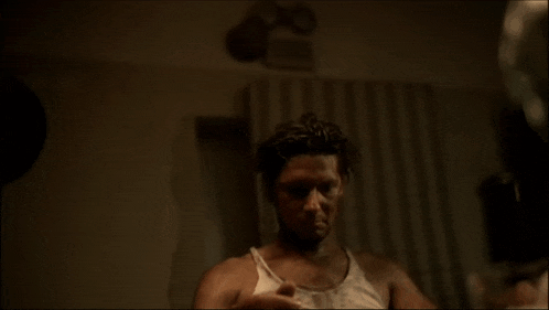 a man in a tank top is looking at himself in a mirror