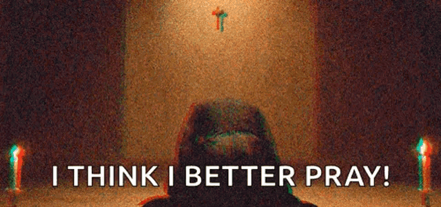 a man is kneeling down in front of a cross and candles in a dark room .