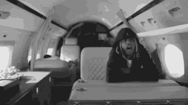 a black and white photo of a man in a hooded jacket on a plane