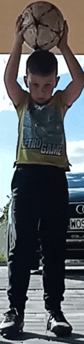 a young boy in a retro game shirt holds a soccer ball above his head