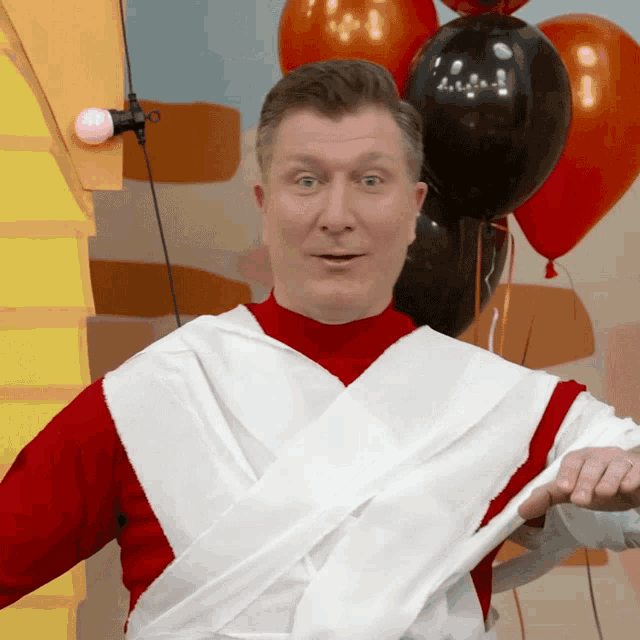 a man is wrapped in toilet paper and balloons are behind him