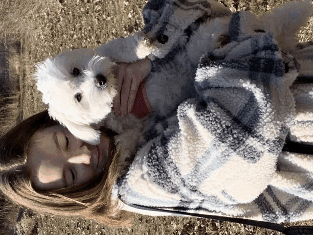 a woman is wrapped in a blanket and holding a small white dog