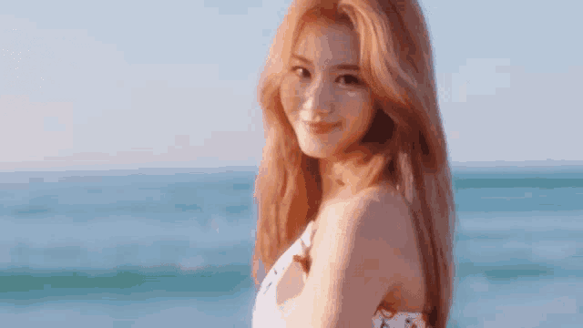 a woman in a white dress is standing on the beach near the ocean .