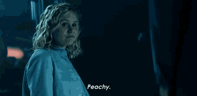 a woman in a blue shirt says " peachy " in a dark room