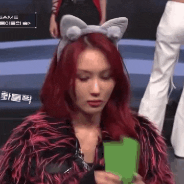 a woman with red hair is wearing a cat ear headband and holding a green object .