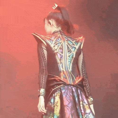a woman in a colorful dress is standing on a stage in front of a red light .