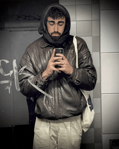 a man in a leather jacket takes a picture of himself in a mirror