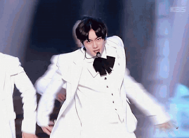 a man in a white suit with a bow tie is dancing on a stage .