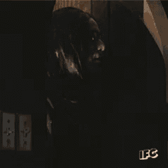 a man with long black hair and glasses is standing in a dark room with a sign that says ifc