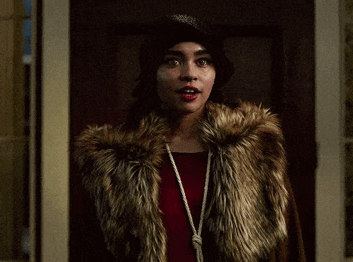 a woman wearing a fur coat and a red dress is standing in front of a door .