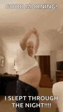 a man with a very large belly is standing in a living room with his arms up .