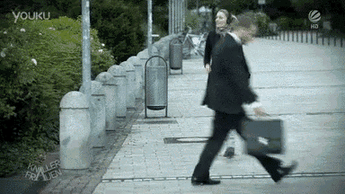 a man in a suit carrying a briefcase is walking down a sidewalk with a woman behind him ..