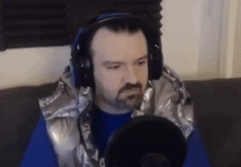 a man with a beard is wearing headphones and a vest while sitting on a couch .