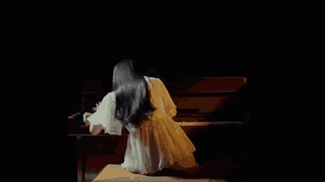 a woman in a white dress is kneeling down in front of a piano in a dark room .