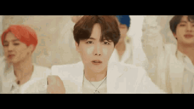 a group of young men are dancing together in a room and one of them is wearing a white jacket .
