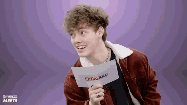 a young man holding a piece of paper that says pop buzz on it