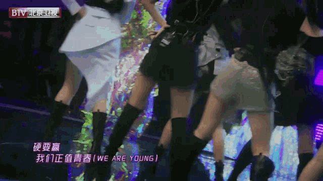 a group of women are dancing on a stage with the words we are young in the corner