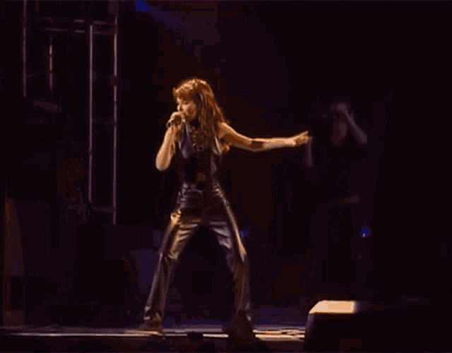 a woman is standing on a stage holding a microphone and dancing .