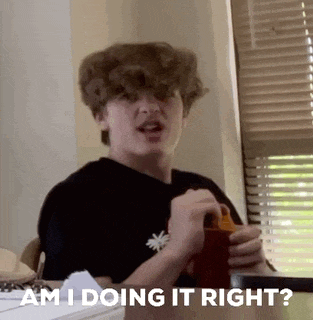 a young man is sitting at a table holding a cup and saying `` am i doing it right? ''