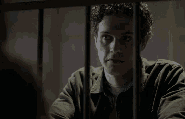 a man with curly hair is behind bars and looking at something