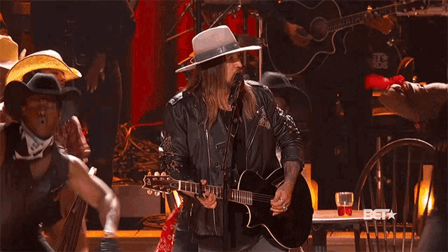 a man in a cowboy hat playing a guitar in front of a bet logo