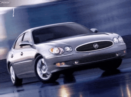 a silver buick is driving down a wet road