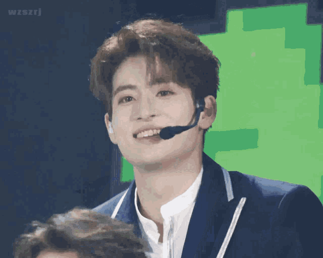 a young man wearing a microphone and a suit smiles
