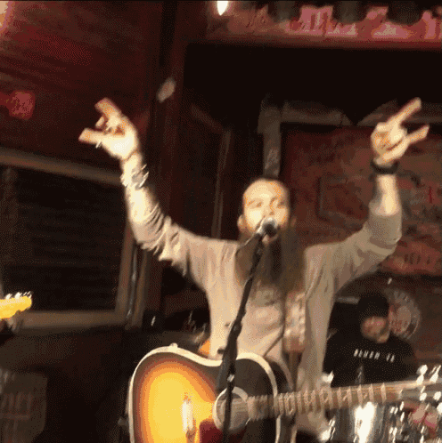 a man playing a guitar and singing into a microphone with his arms in the air