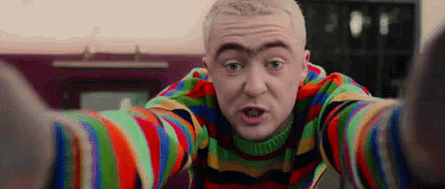 a man wearing a colorful sweater is taking a selfie
