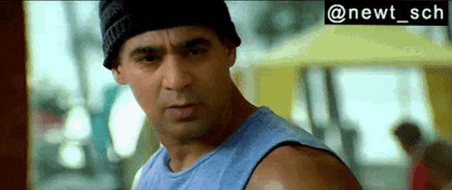 a man wearing a blue tank top and a black beanie is looking at the camera .