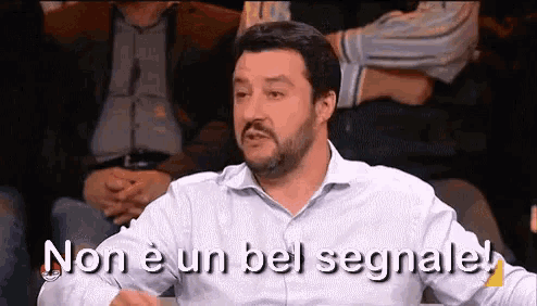a man with a beard is sitting in a crowd and says non e un bel segnale .